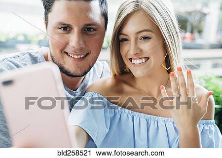 Caucasian couple posing for cell phone selfie showing engagement ring View Large Photo Image Stock Image - Caucasian couple posing for cell phone selfie showing engagement ring. Fotosearch