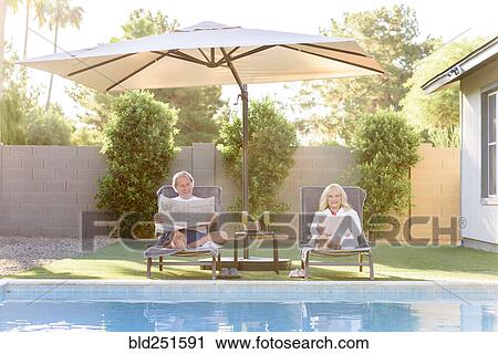 Caucasian couple reading newspaper and using laptop near swimming pool View Large Photo Image Stock Image - Caucasian couple reading newspaper and using laptop near swimming pool. Fotosearch