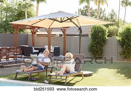 Caucasian couple reading newspaper and using laptop near swimming pool View Large Photo Image Stock Image - Caucasian couple reading newspaper and using laptop near swimming pool. Fotosearch