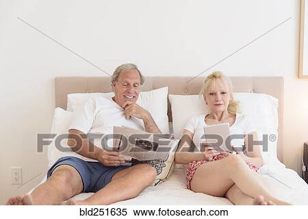 Caucasian couple reading newspaper and digital tablet in bed View Large Photo Image Stock Photography - Caucasian couple reading newspaper and digital tablet in bed. Fotosearch