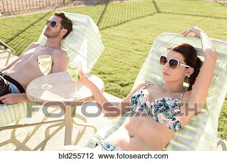 Stock Image - Caucasian couple relaxing in lounge chairs. Fotosearch