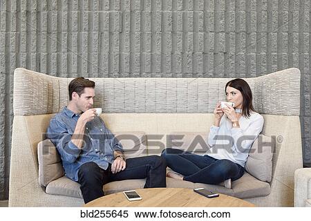 Stock Photography - Caucasian couple relaxing on sofa drinking coffee. Fotosearch