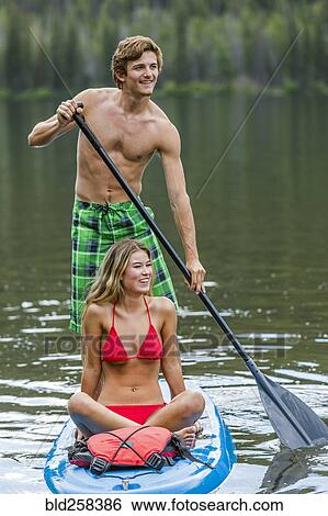 Stock Photograph - Caucasian couple riding paddleboard. Fotosearch
