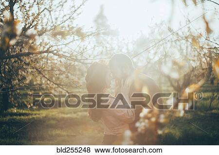 Stock Photo - Caucasian couple rubbing noses near trees. Fotosearch