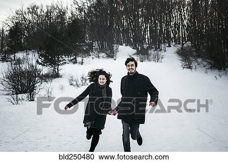 Stock Image - Caucasian couple running from forest in winter. Fotosearch