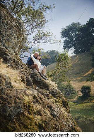 Stock Image - Caucasian couple sitting on hill near river. Fotosearch