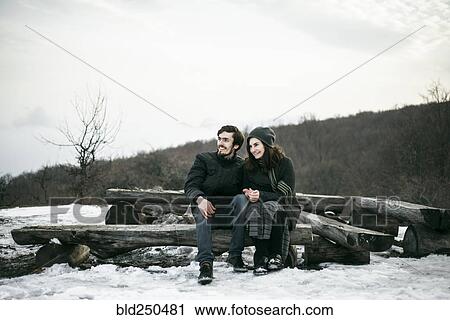 Stock Image - Caucasian couple sitting on logs in winter. Fotosearch