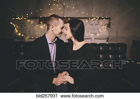 Stock Image - Caucasian couple sitting on sofa rubbing noses. Fotosearch