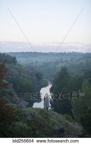 Picture - Caucasian couple standing on hill admiring river. Fotosearch