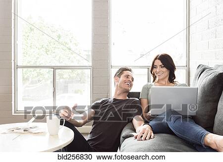 Stock Image - Caucasian couple using laptop on sofa. Fotosearch