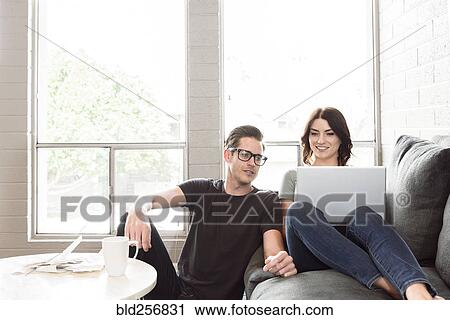 Stock Image - Caucasian couple using laptop on sofa. Fotosearch
