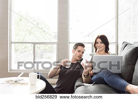 Stock Photo - Caucasian couple using laptop on sofa. Fotosearch