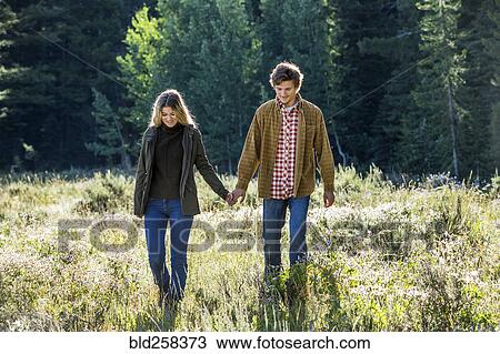 Stock Image - Caucasian couple walking in field holding hands. Fotosearch