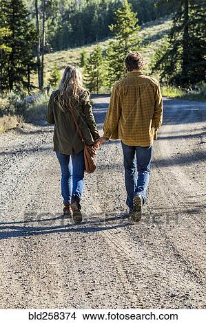 Picture - Caucasian couple walking on dirt road holding hands. Fotosearch