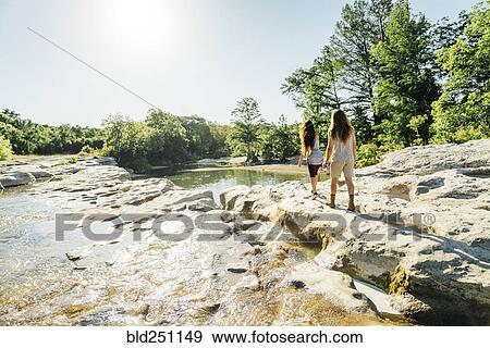 Stock Photo - Caucasian couple walking on rocks near river. Fotosearch