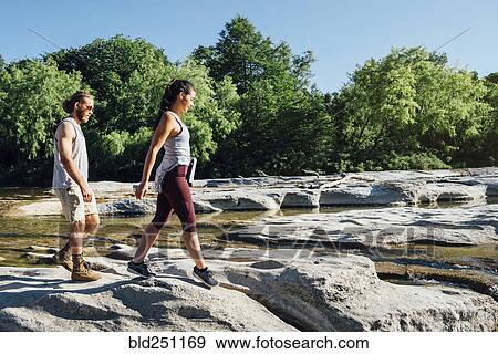 Stock Photo - Caucasian couple walking on rocks near river. Fotosearch