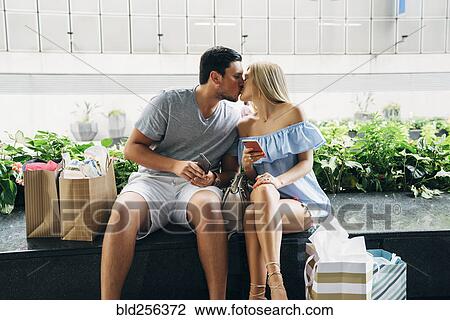 Caucasian couple with shopping bags and cell phones kissing View Large Photo Image Stock Image - Caucasian couple with shopping bags and cell phones kissing. Fotosearch