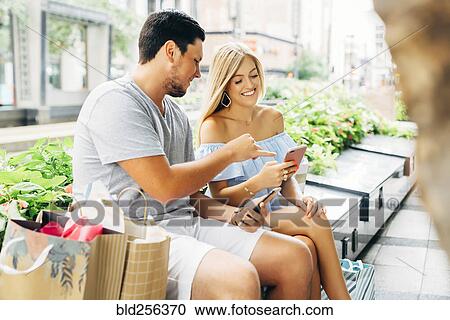 Caucasian couple with shopping bags texting on cell phones View Large Photo Image Stock Image - Caucasian couple with shopping bags texting on cell phones. Fotosearch