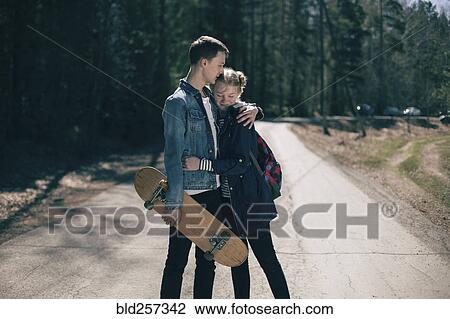 Stock Image - Caucasian couple with skateboard hugging in road. Fotosearch