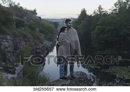 Caucasian couple wrapped in blanket standing on rock near river View Large Photo Image Stock Photo - Caucasian couple wrapped in blanket standing on rock near river. Fotosearch