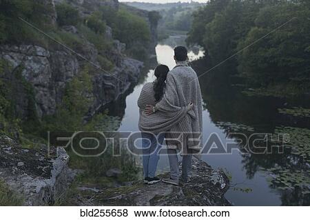 Caucasian couple wrapped in blanket standing on rock admiring river View Large Photo Image Stock Photo - Caucasian couple wrapped in blanket standing on rock admiring river. Fotosearch