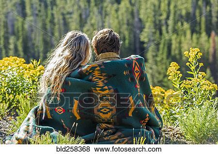 Stock Photo - Caucasian couple wrapped in blanket admiring scenic view of landscape. Fotosearch
