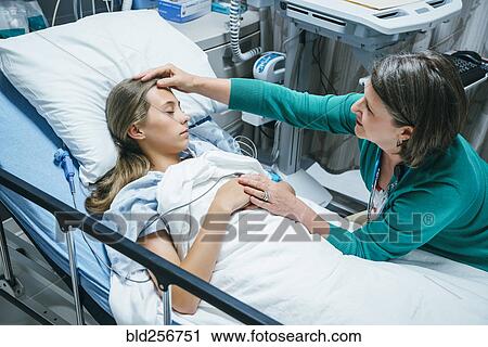 Stock Image - Caucasian doctor comforting patient in hospital bed. Fotosearch