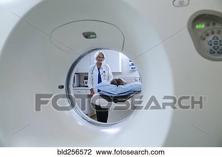 Stock Image - Caucasian doctor comforting patient near scanner. Fotosearch