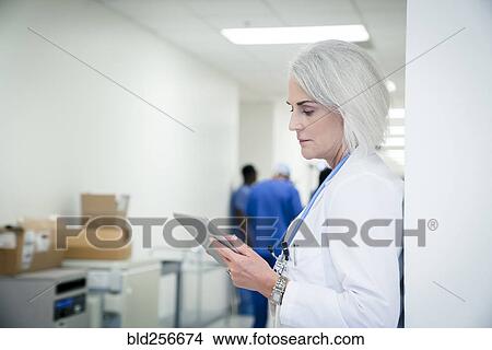 Caucasian doctor leaning on wall using digital tablet View Large Photo Image Picture - Caucasian doctor leaning on wall using digital tablet. Fotosearch