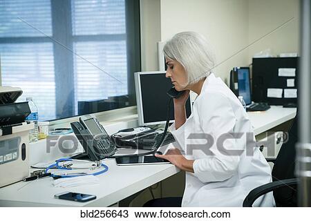 Stock Image - Caucasian doctor talking on telephone and using digital tablet. Fotosearch