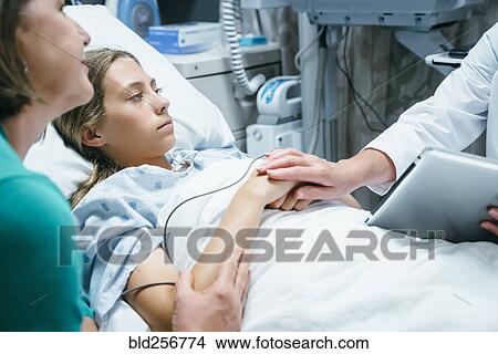 Picture - Caucasian doctor with digital tablet comforting girl in hospital bed. Fotosearch