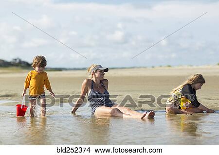 Picture - Caucasian families sitting in waves on the beach. Fotosearch