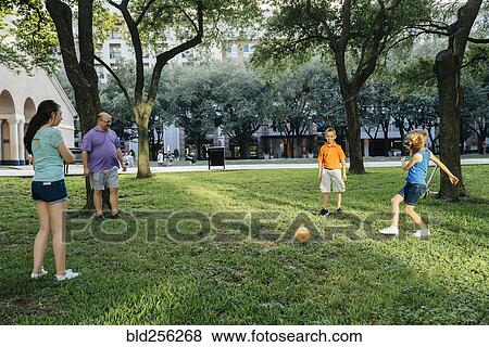 Stock Photo - Caucasian family kicking soccer ball in park. Fotosearch
