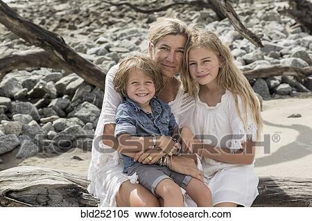Stock Photography - Caucasian family sitting on driftwood at beach. Fotosearch