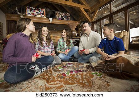 Stock Image - Caucasian family sitting on rug playing card game. Fotosearch