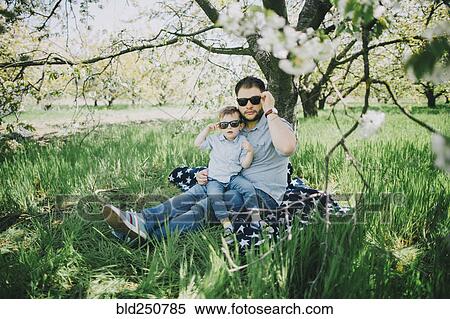 Stock Photography - Caucasian father and son wearing sunglasses on blanket in grass. Fotosearch