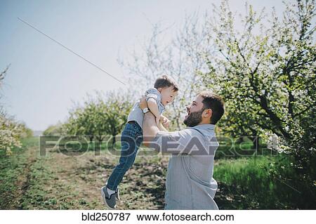 Caucasian father lifting son near tree View Large Photo Image Stock Photo - Caucasian father lifting son near tree. Fotosearch