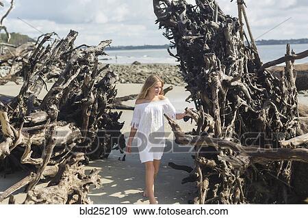 Stock Photo - Caucasian girl admiring driftwood on beach. Fotosearch
