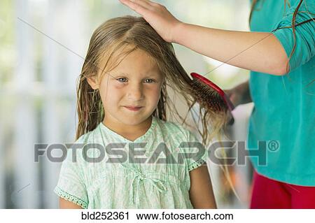 Stock Image - Caucasian girl brushing wet hair of sister. Fotosearch