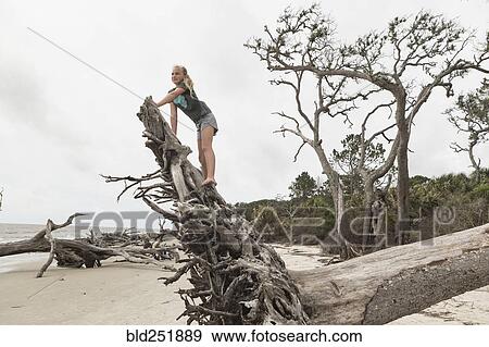 Stock Photo - Caucasian girl climbing on driftwood on beach. Fotosearch