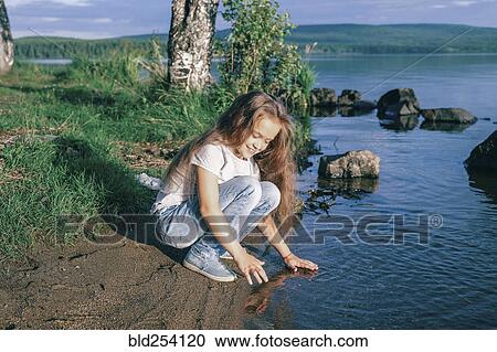 Stock Image - Caucasian girl crouching near river. Fotosearch