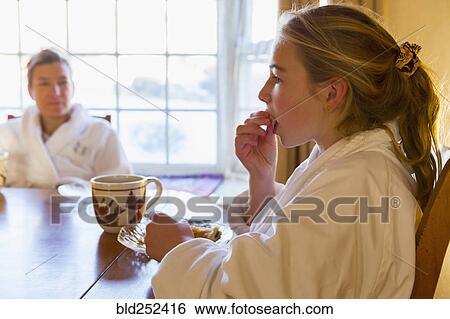 Stock Photograph - Caucasian girl eating breakfast in bathrobe. Fotosearch