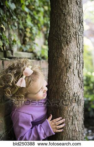 Stock Photo - Caucasian girl hiding behind tree trunk. Fotosearch
