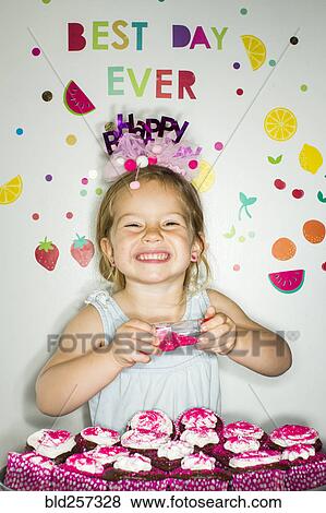 Stock Photo - Caucasian girl holding s1inkles over tray of cupcakes for birthday. Fotosearch