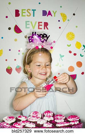 Stock Photo - Caucasian girl holding s1inkles over tray of cupcakes for birthday. Fotosearch