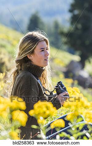 Stock Image - Caucasian girl in field holding binoculars. Fotosearch