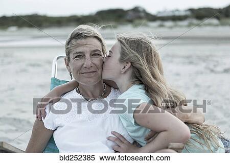 Stock Photography - Caucasian girl kissing mother on cheek at windy beach. Fotosearch