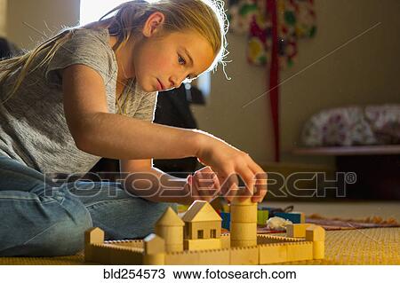 Stock Image - Caucasian girl kneeling on the floor building toys castle. Fotosearch