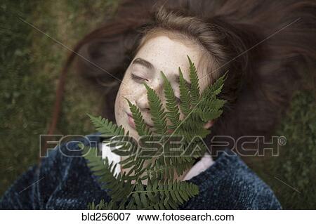Stock Photo - Caucasian girl laying in grass holding branch. Fotosearch