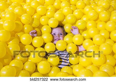 Stock Image - Caucasian girl laying in pile of yellow balls. Fotosearch
